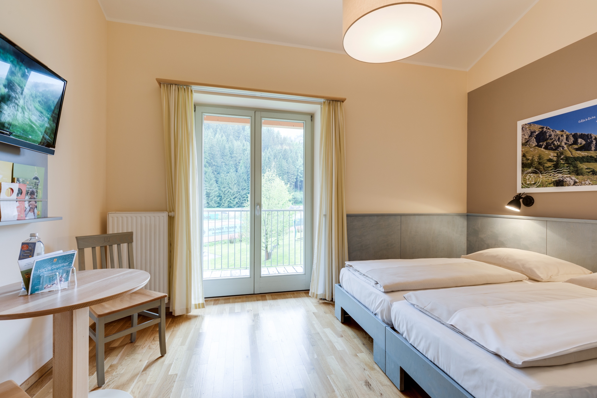Doppelbett im Doppelzimmer im JUFA Hotel Veitsch mit Blick auf den Balkon. JUFA Hotels bietet kinderfreundlichen und erlebnisreichen Urlaub für die ganze Familie.