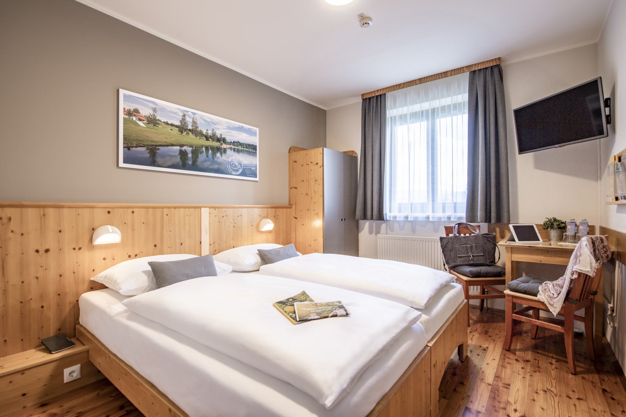 Ihr seht ein Doppelbett in einem Doppelzimmer im JUFA Hotel Maria Lankowitz mit Wandbild. JUFA Hotels bietet tollen Sommerurlaub an schönen Seen für die ganze Familie.