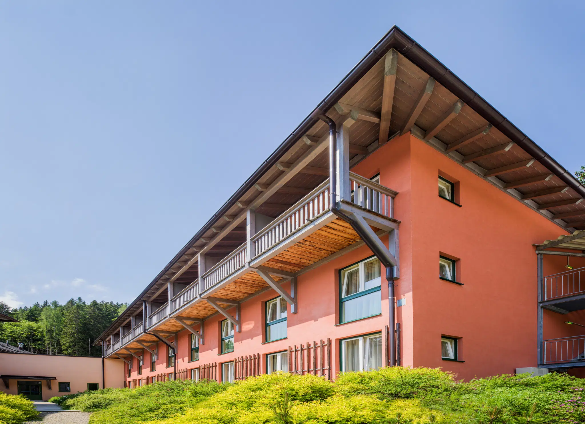 Ihr seht die Hotelansicht im Sommer mit grünen Bäumen und Sträuchern vom JUFA Hotel Altaussee***. Der Ort für erlebnisreichen Natururlaub für die ganze Familie.