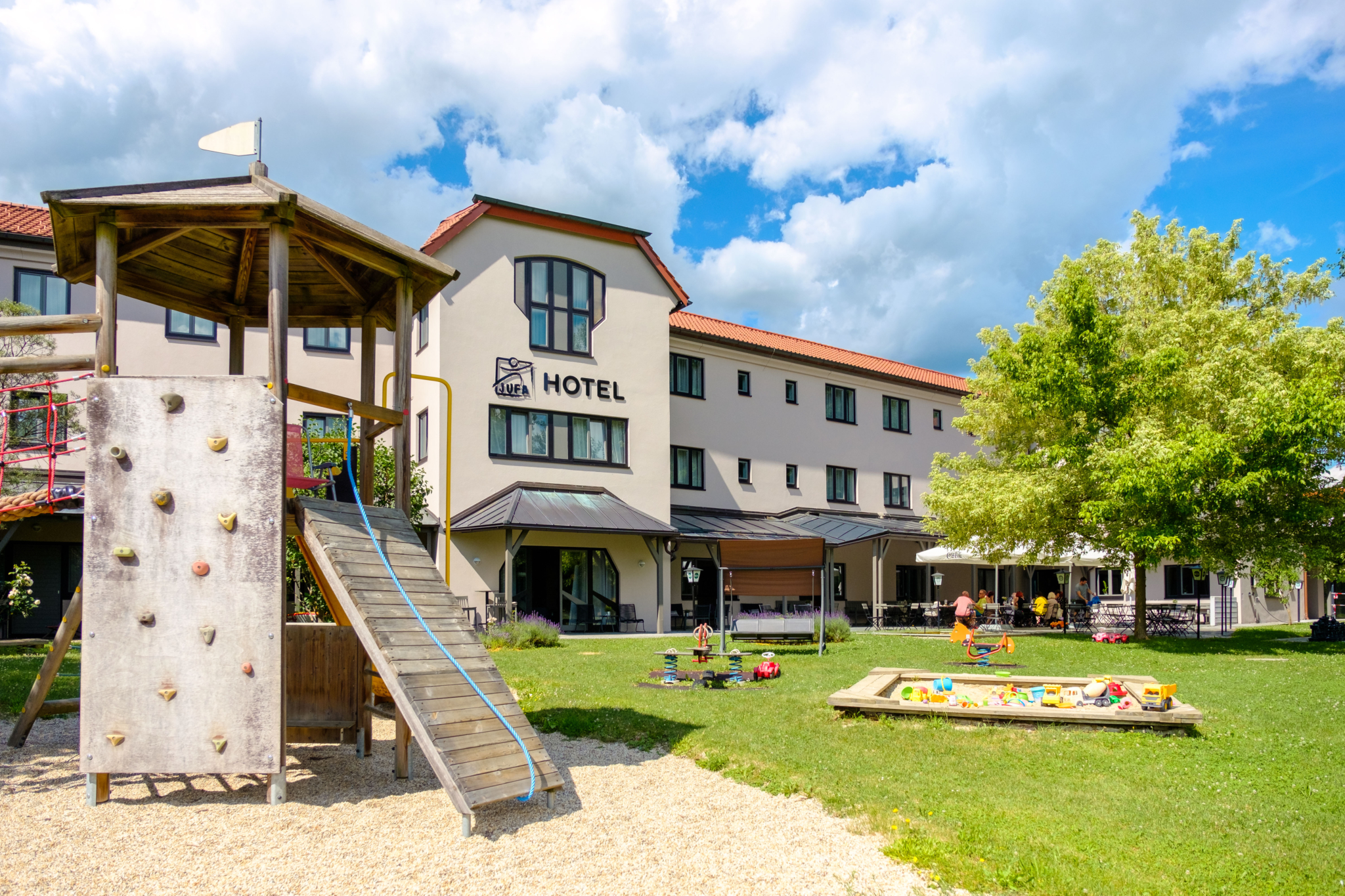 Ihr seht das JUFA Hotel Lipizzanerheimat von Aussen mit Garten und Spielplatz. JUFA Hotels bietet kinderfreundlichen und erlebnisreichen Urlaub für die ganze Familie.
