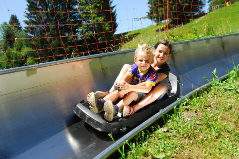 Ihr seht Kinder auf der Sommerrodelbahn in Laterns. Die JUFA Hotels bieten erholsamen Urlaub für die ganze Familie.