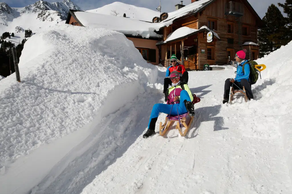 Ihr seht Erwachsene beim Schneeschuhrodeln bei Sonnenschein auf einer Berghütte im Murtal. JUFA Hotels bietet erholsamen Familienurlaub und einen unvergesslichen Winterurlaub.
