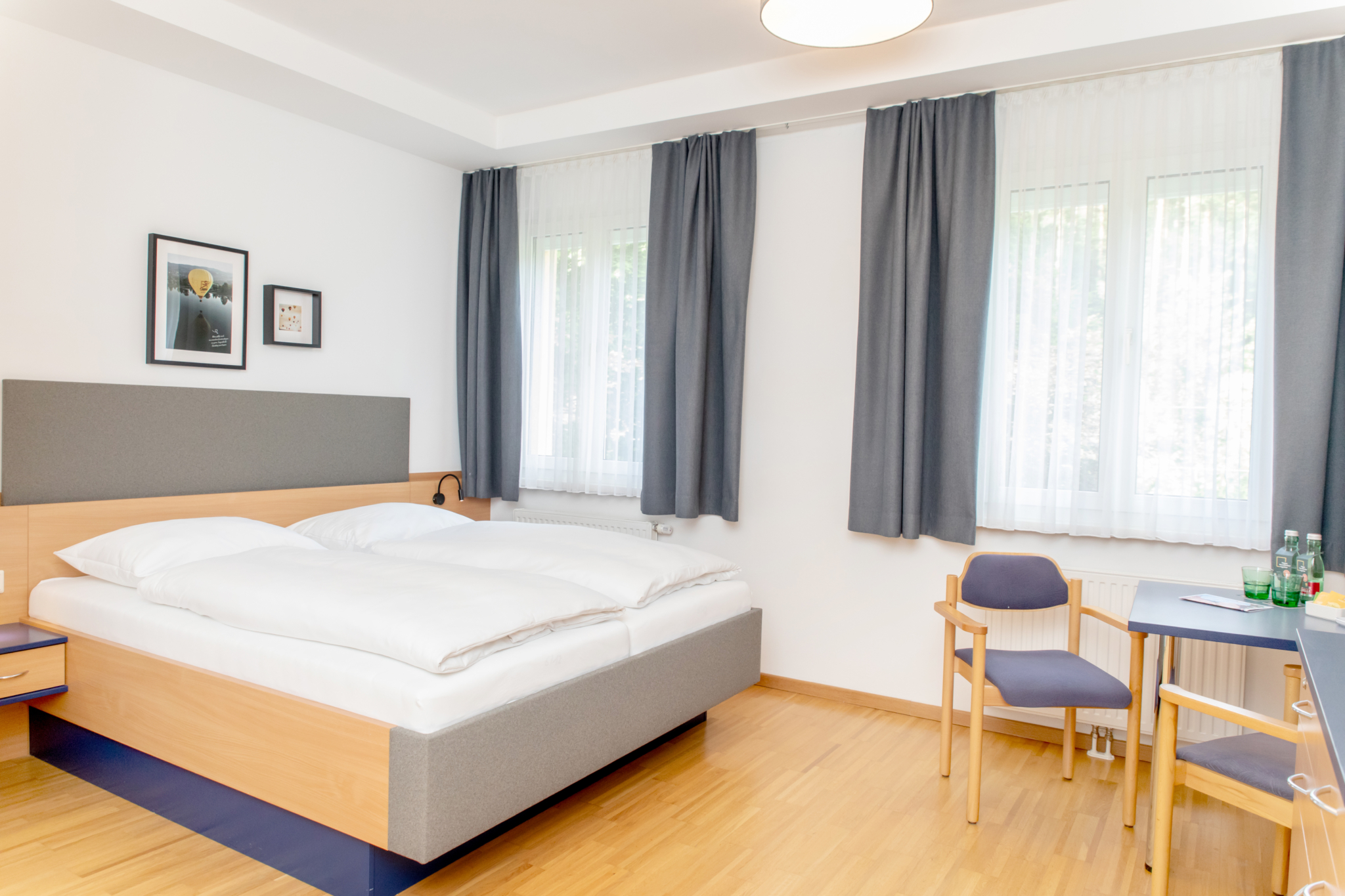 Ihr seht ein Bild vom Doppelzimmer mit Doppelbett, Vorhängen sowie Sitzecke mit Tisch im JUFA Hotel Garni Stubenberg.