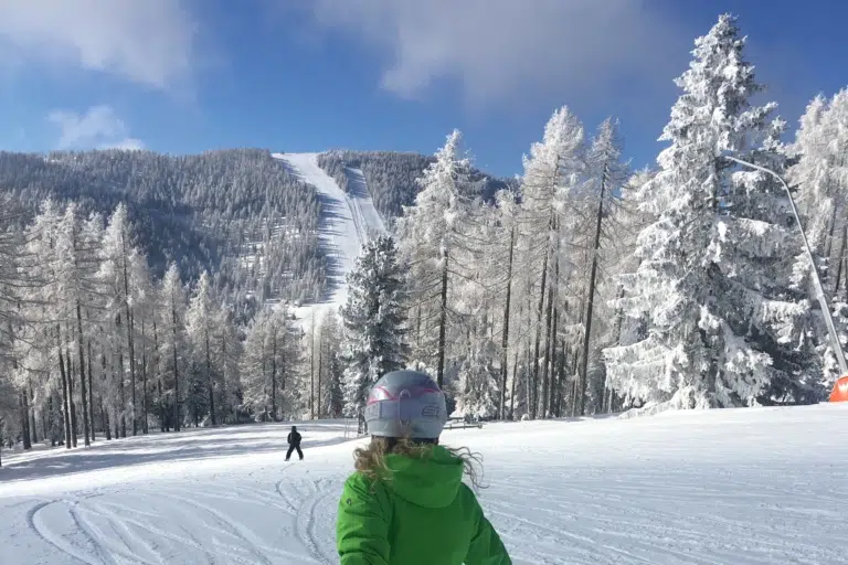 Ihr seht eine Person von hinten beim Skifahren auf der Hochrindl im Winter.