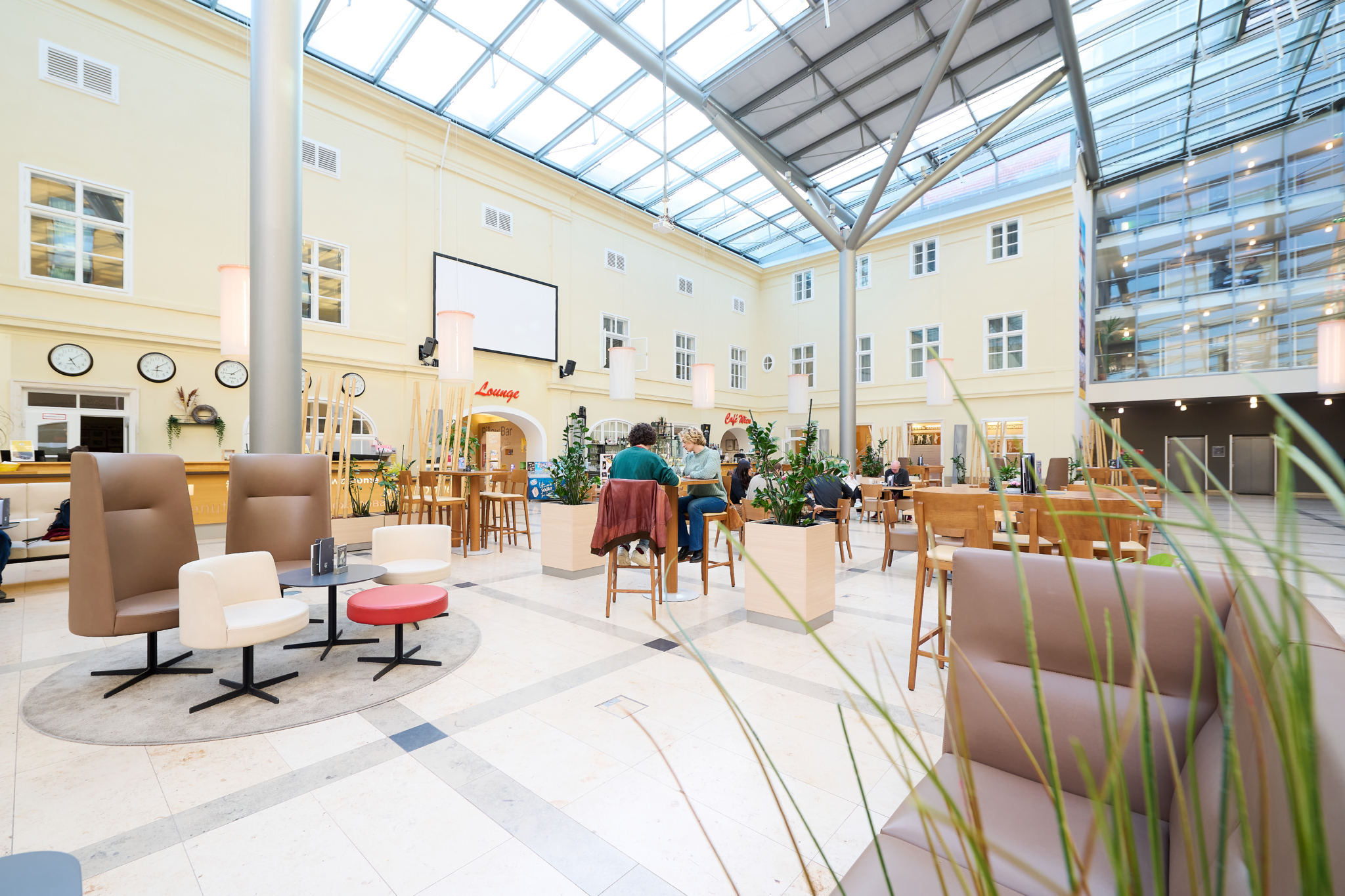 Ihr seht das Atrium im JUFA Hotel Wien City mit rotem Glasdach. JUFA Hotels bietet erlebnisreichen Städtetrip für die ganze Familie und den idealen Platz für Seminare