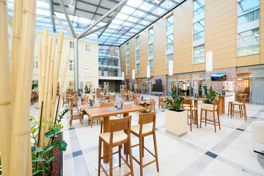 Ihr seht das Atrium im JUFA Hotel Wien City mit blauem Glasdach. JUFA Hotels bietet erlebnisreichen Städtetrip für die ganze Familie und den idealen Platz für Ihr Seminar.