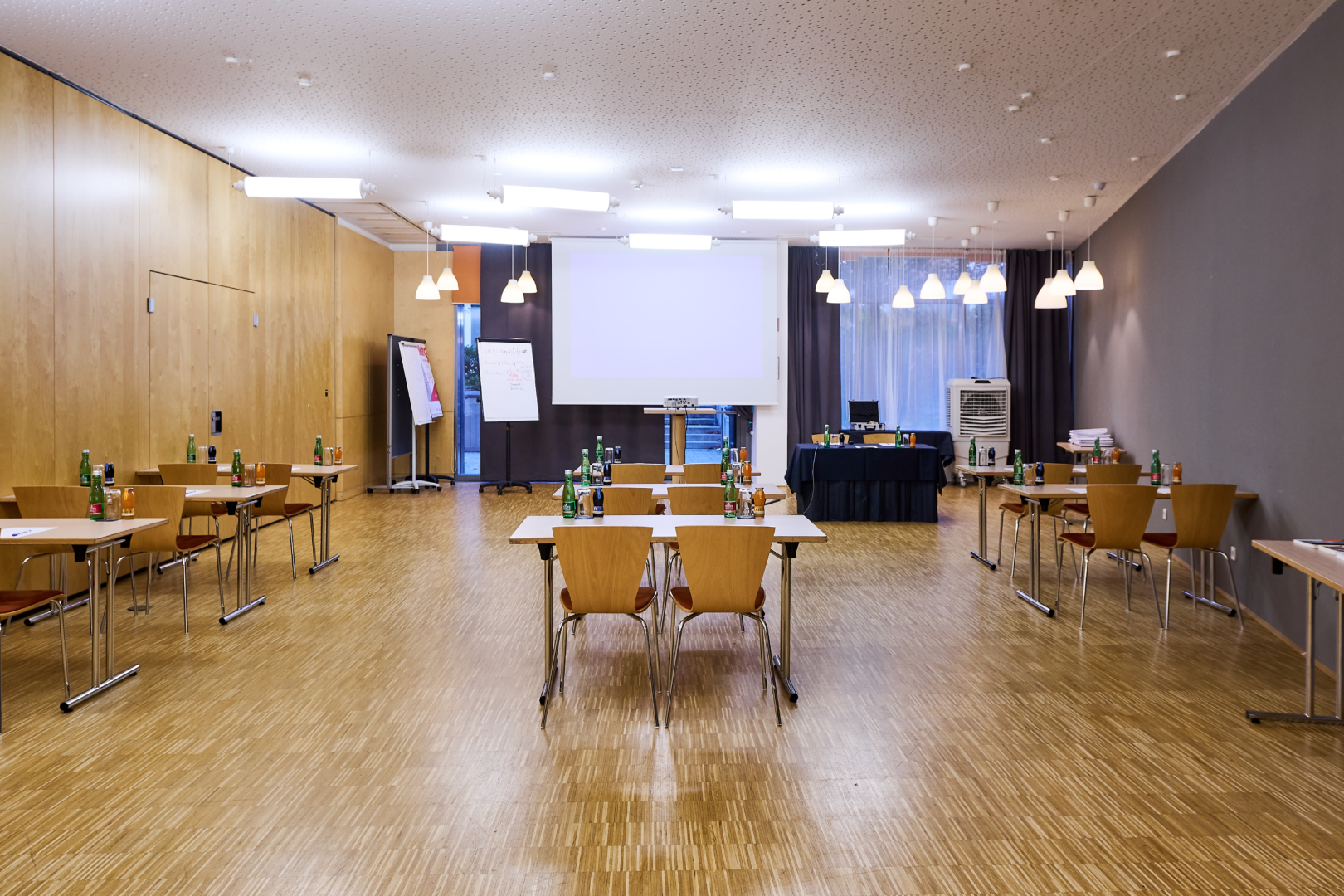 Ihr seht den Seminarraum Flamenco im JUFA Hotel Wien City****. Der Raum ist gefüllt mit Sesseln und Tischen. Auf den Tischen befinden sich Blöcke, Stifte und Getränke. Im Hintergrund ist ein Beamer, eine Leinwand und ein Flipchart.Der Ort für eure erfolgreichen Seminare, Workshops und Tagungen.