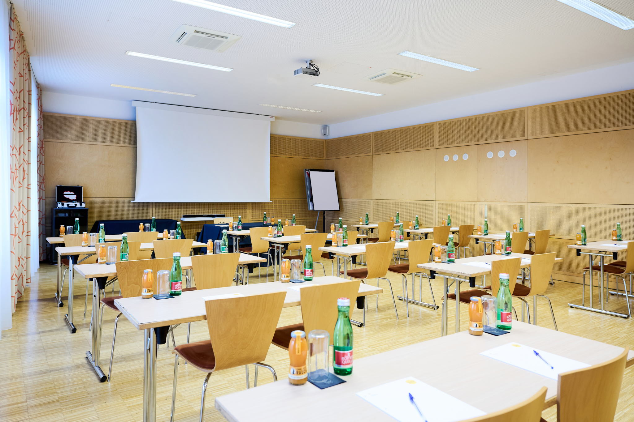 Ihr seht den Seminarraum Symphonia im JUFA Hotel Wien City****. Der Raum ist gefüllt mit Sesseln und Tischen. Auf den Tischen befinden sich Blöcke, Stifte und Getränke. Im Hintergrund ist ein Beamer, eine Leinwand und ein Flipchart. Der Ort für eure erfolgreichen Seminare, Workshops und Tagungen.
