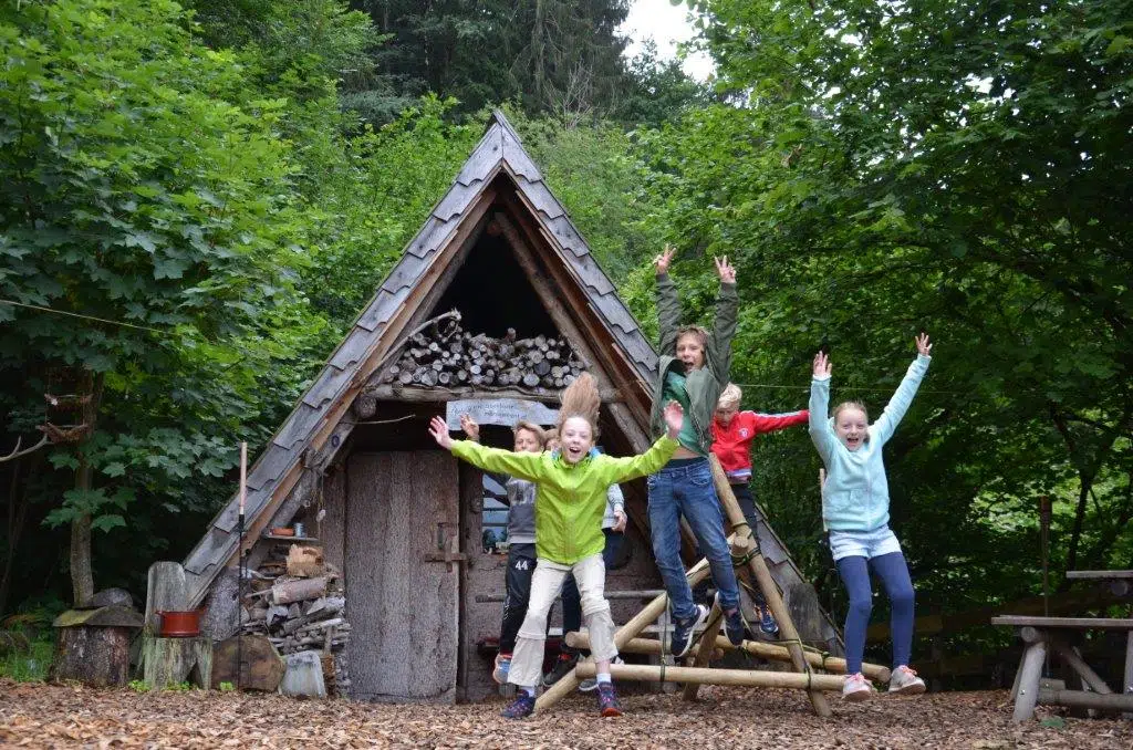 Ihr seht eine Gruppe von Kindern beim Abenteuercamp springend und lachend.